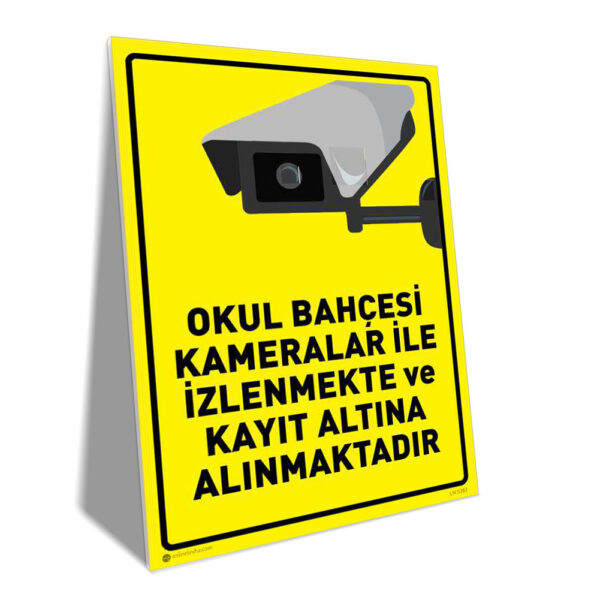 Yellow warning sign with a CCTV camera illustration and Turkish text warning that the school yard is under surveillance and recording.